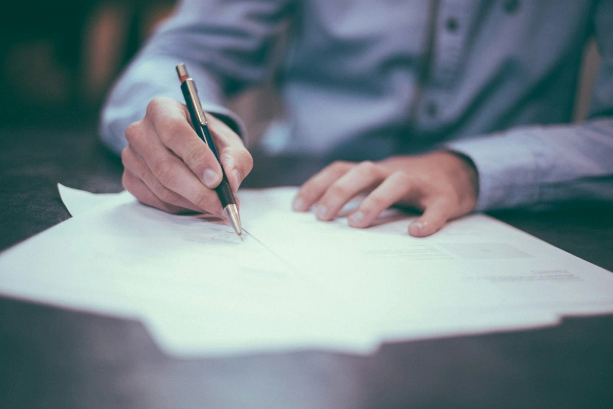 Persona firmando documentos legales sobre un escritorio